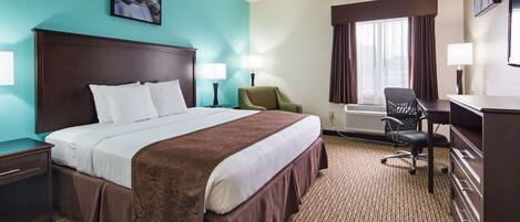 A hotel room with a large bed, two bedside tables, a desk, a chair, and a window with curtains.