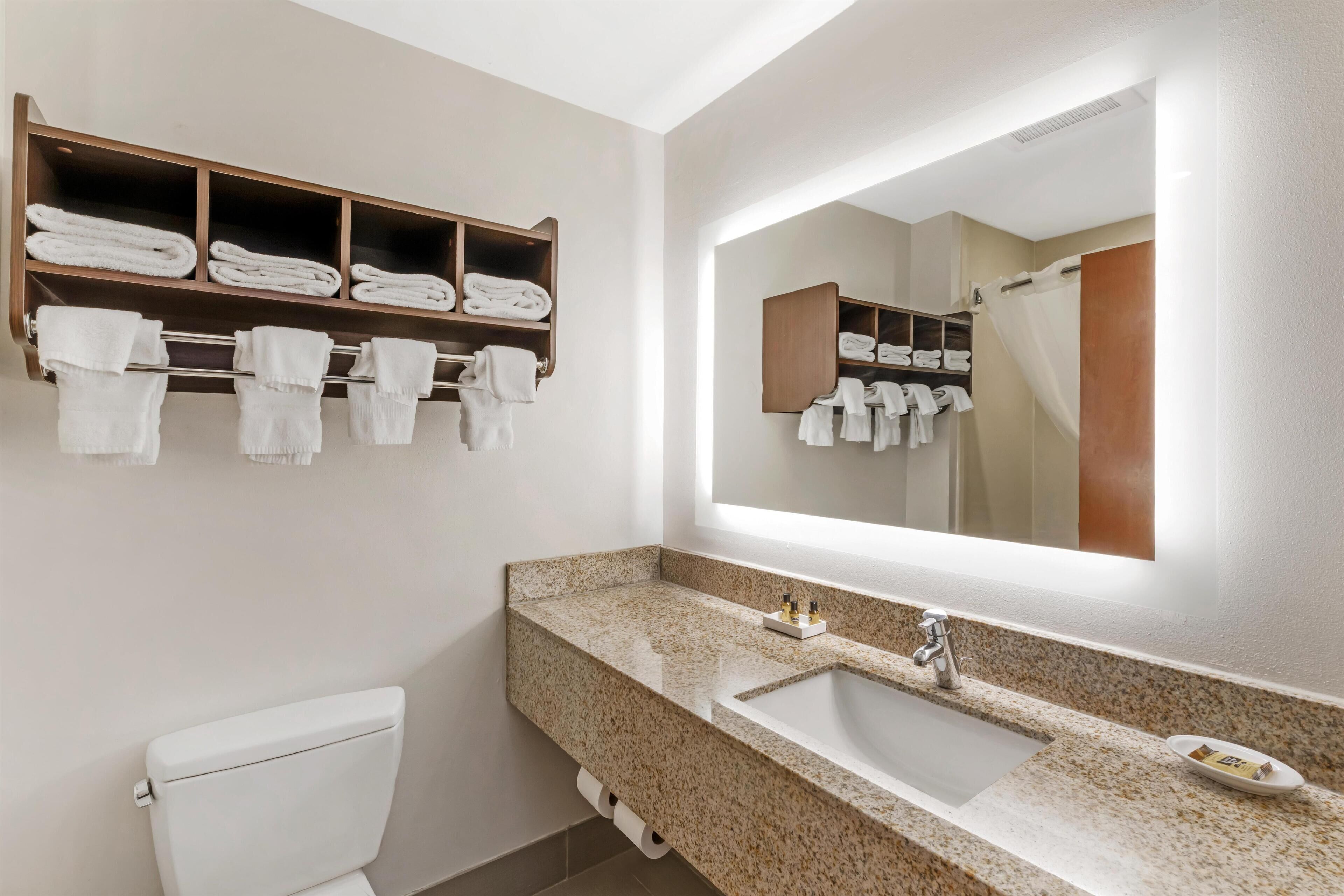 Un baño con lavamanos de encimera de granito, un espejo grande y un perchero con toallas dobladas.