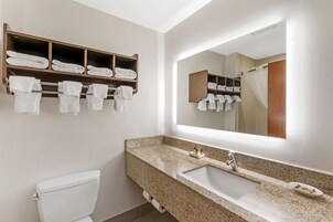 Un baño con lavamanos de encimera de granito, un espejo grande y un perchero con toallas dobladas.