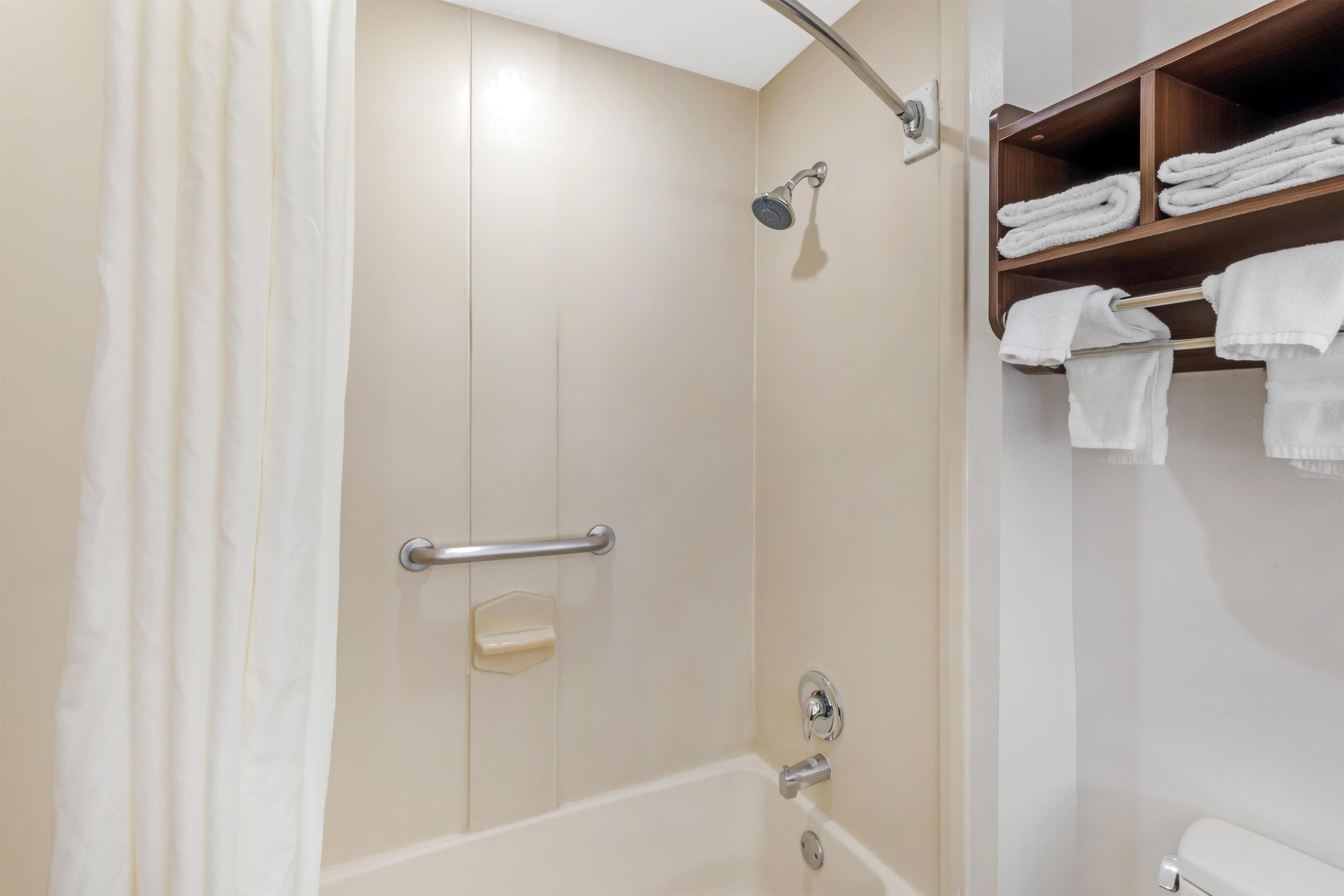 A bathroom with a bathtub, a shower, and a shelf with towels.