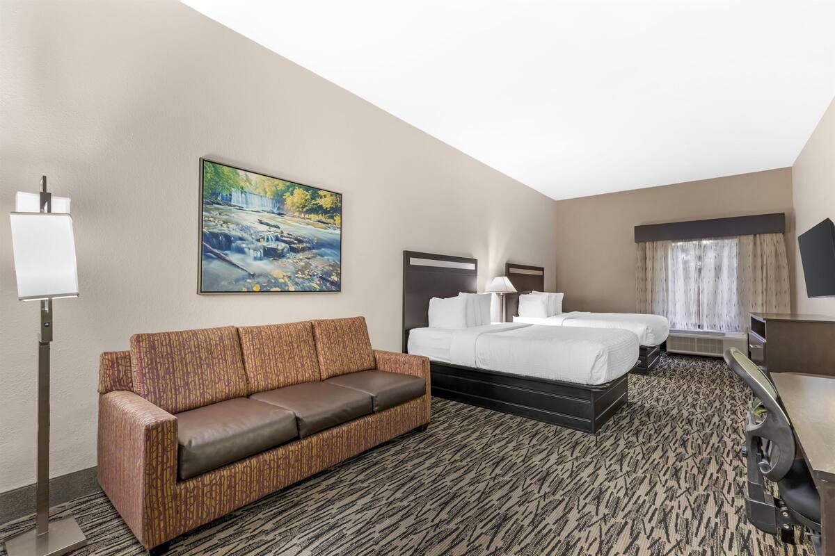 A hotel room with a sofa, a bed, a desk, a lamp, a painting, and a view of a waterfall.