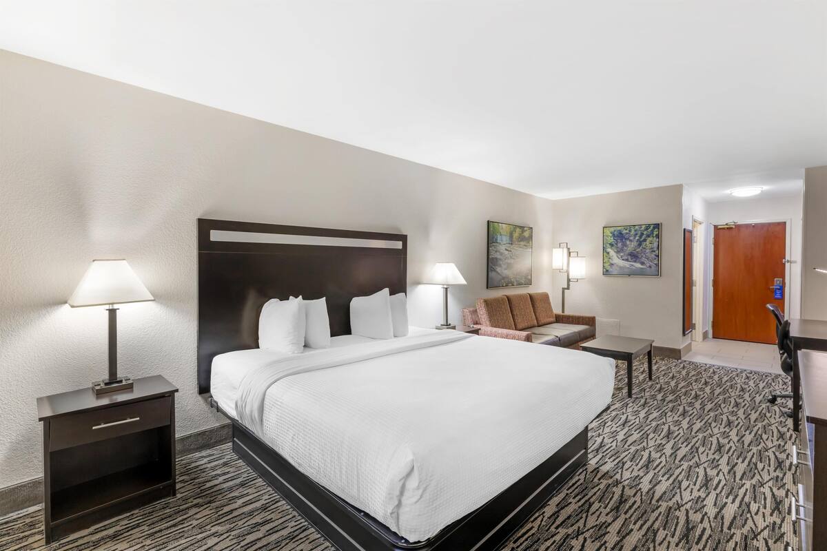 A hotel room with a large bed, two bedside tables with lamps, a chair, a desk, and a door.