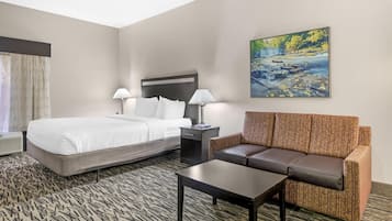 A hotel room with a bed, a sofa, a coffee table, a nightstand with lamps, and a painting of a waterfall.