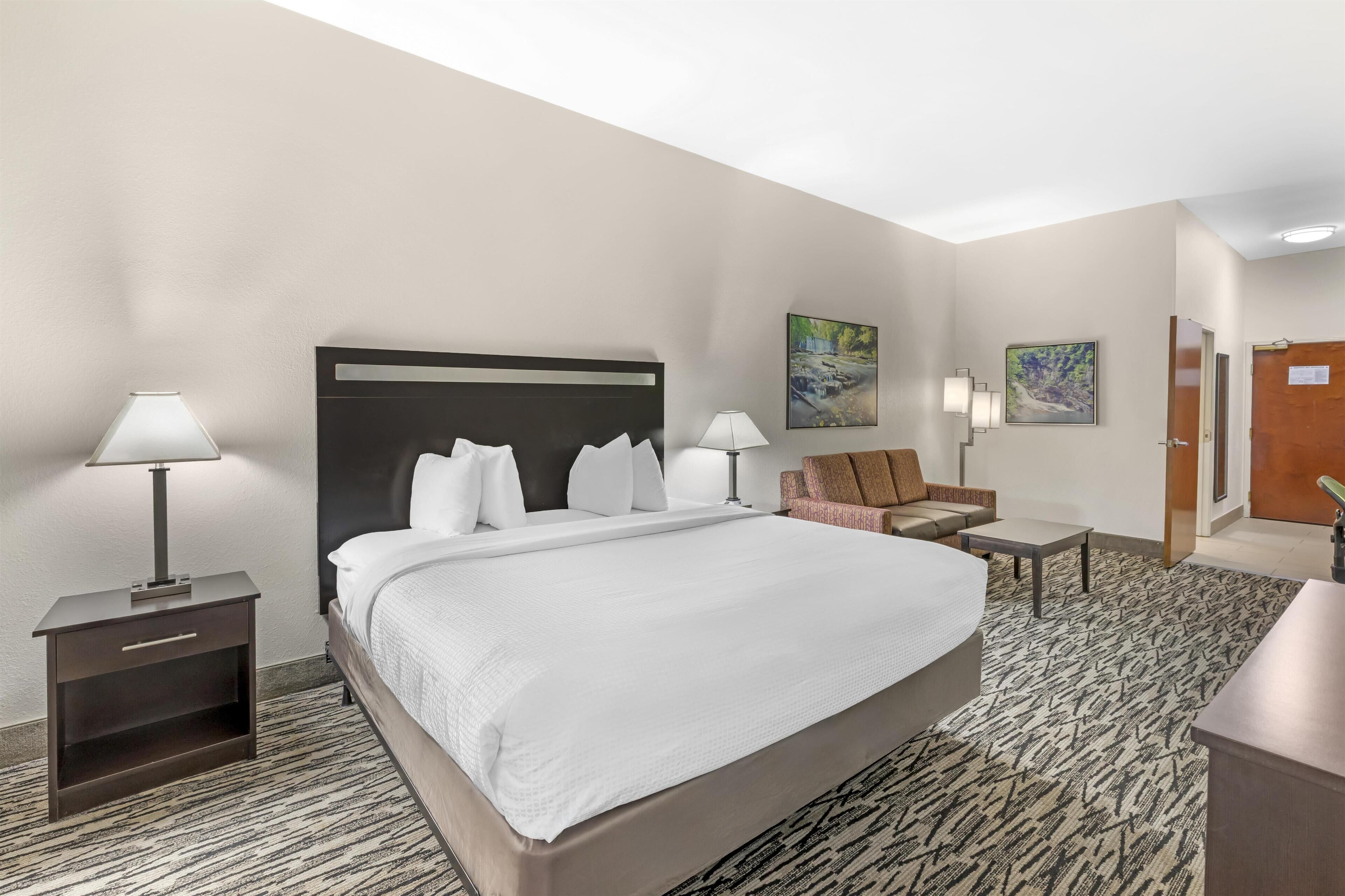A hotel room with a large bed, two bedside tables, a chair, and a desk.