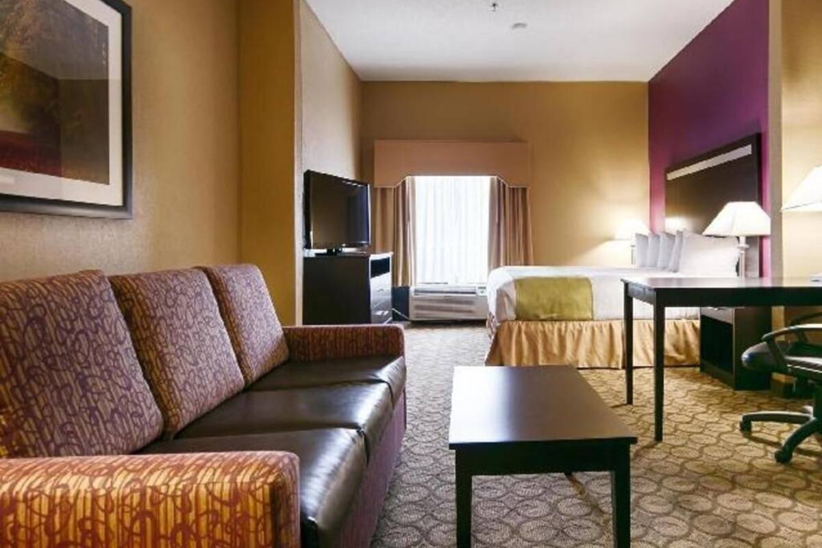 A hotel room with a sofa, a bed, a desk, a television, and a window with curtains.
