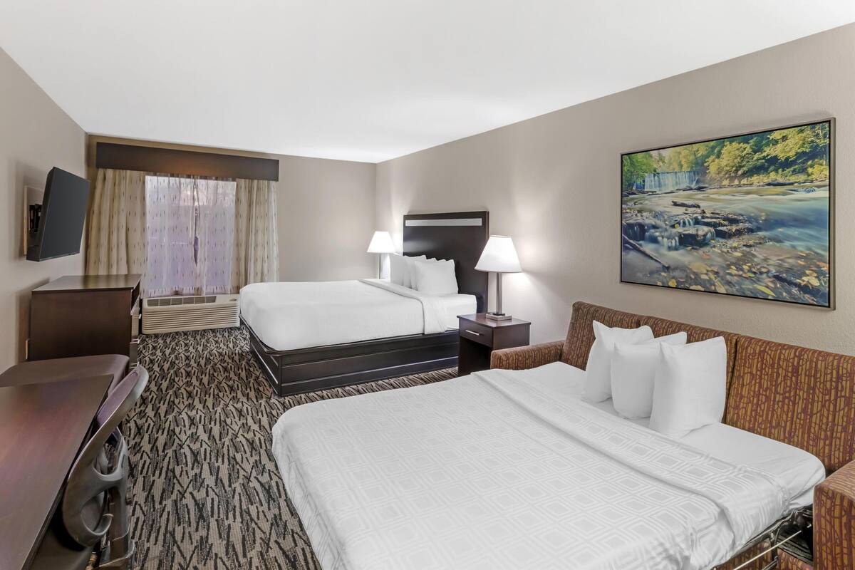 A hotel room with a large bed, a desk, a chair, a TV, and a painting on the wall.