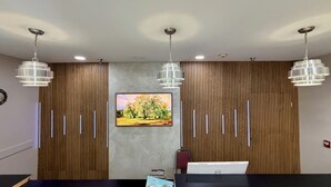 Una sala conferenze con un lungo tavolo, tre lampadari a sospensione, un dipinto paesaggistico incorniciato e un computer Dell sul tavolo.