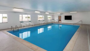 Una piscina interna con acqua cristallina, pareti bianche e pavimento piastrellato.