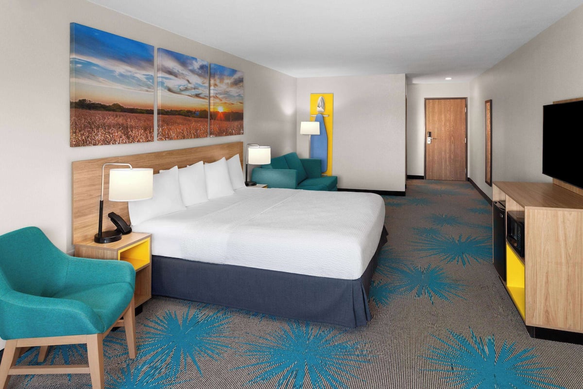 Una habitación de hotel con una cama grande, un escritorio con lámpara, una silla, un televisor y obras de arte en las paredes.