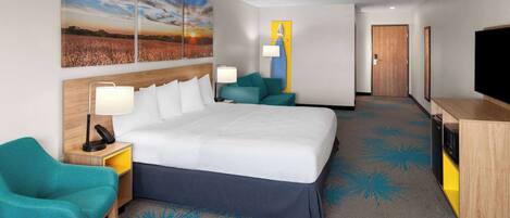 A hotel room with a large bed, a desk with a lamp, a chair, a TV, and artwork on the walls.