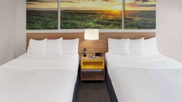 A hotel room with two beds, a nightstand with a lamp, and a wall-mounted painting of a sunset over a field.