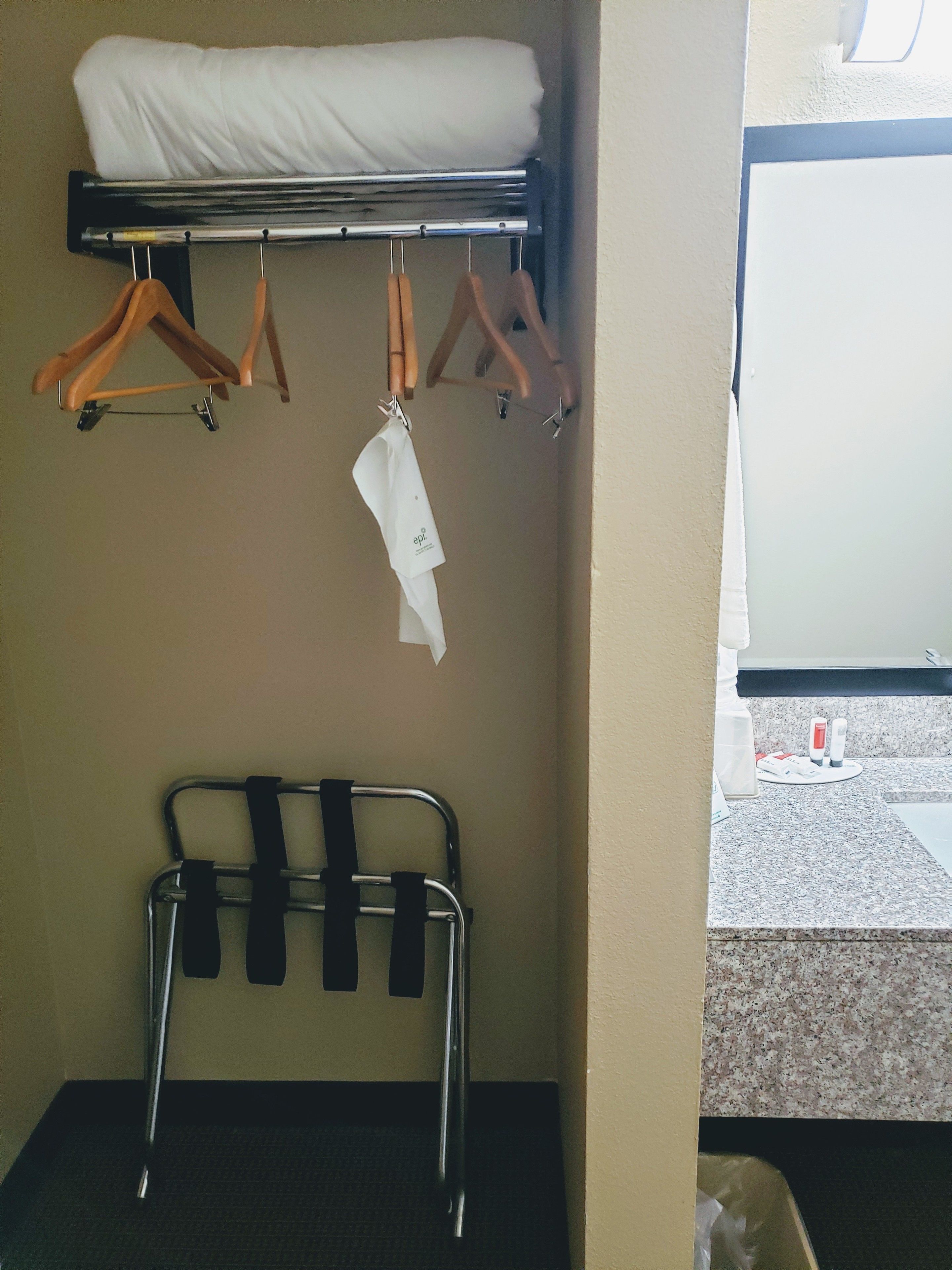 A hotel room with a bed, a metal rack with hangers, and a small table with toiletries.