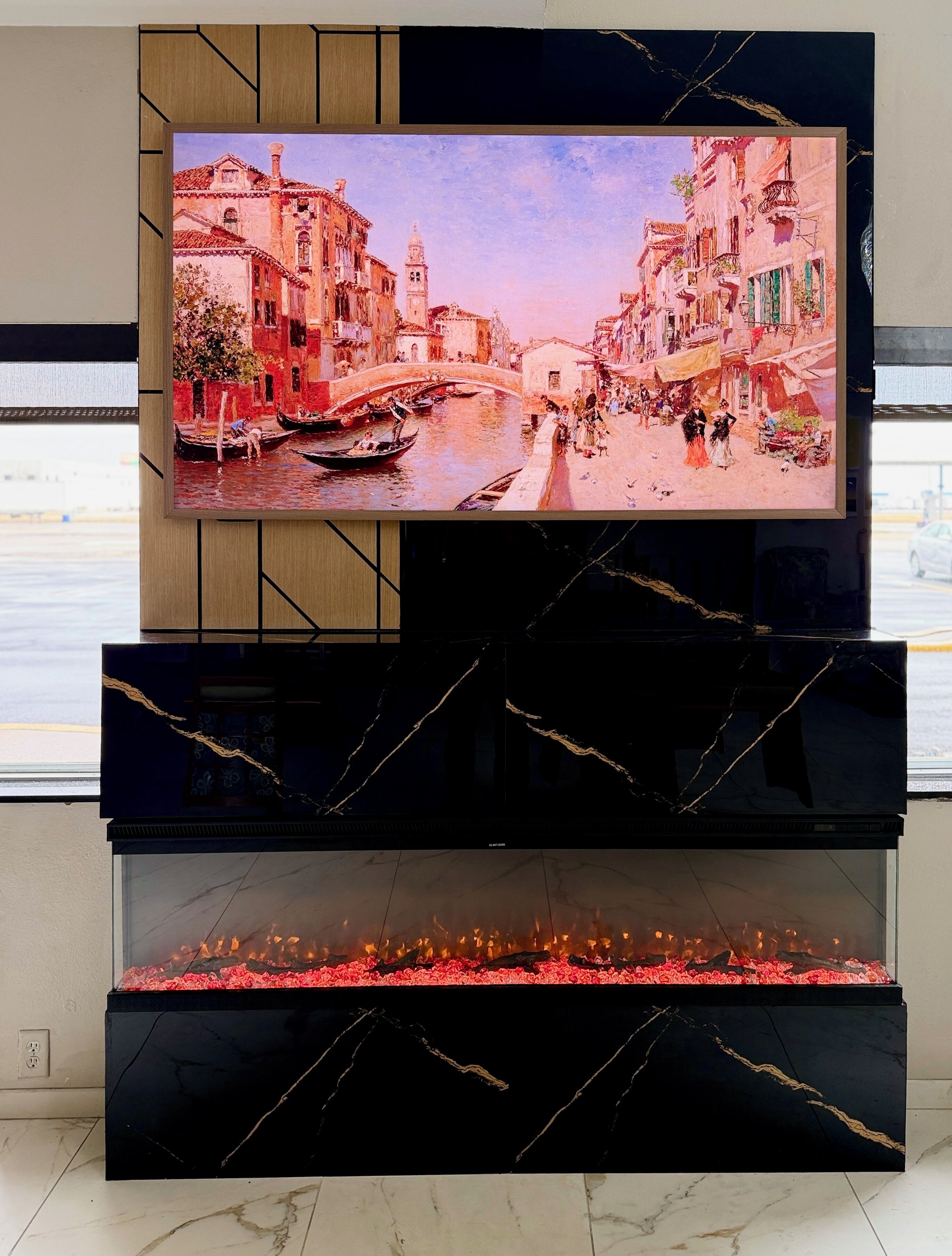 Un téléviseur fixé au-dessus d’une cheminée en marbre noir, avec un tableau représentant une scène d’un canal vénitien.