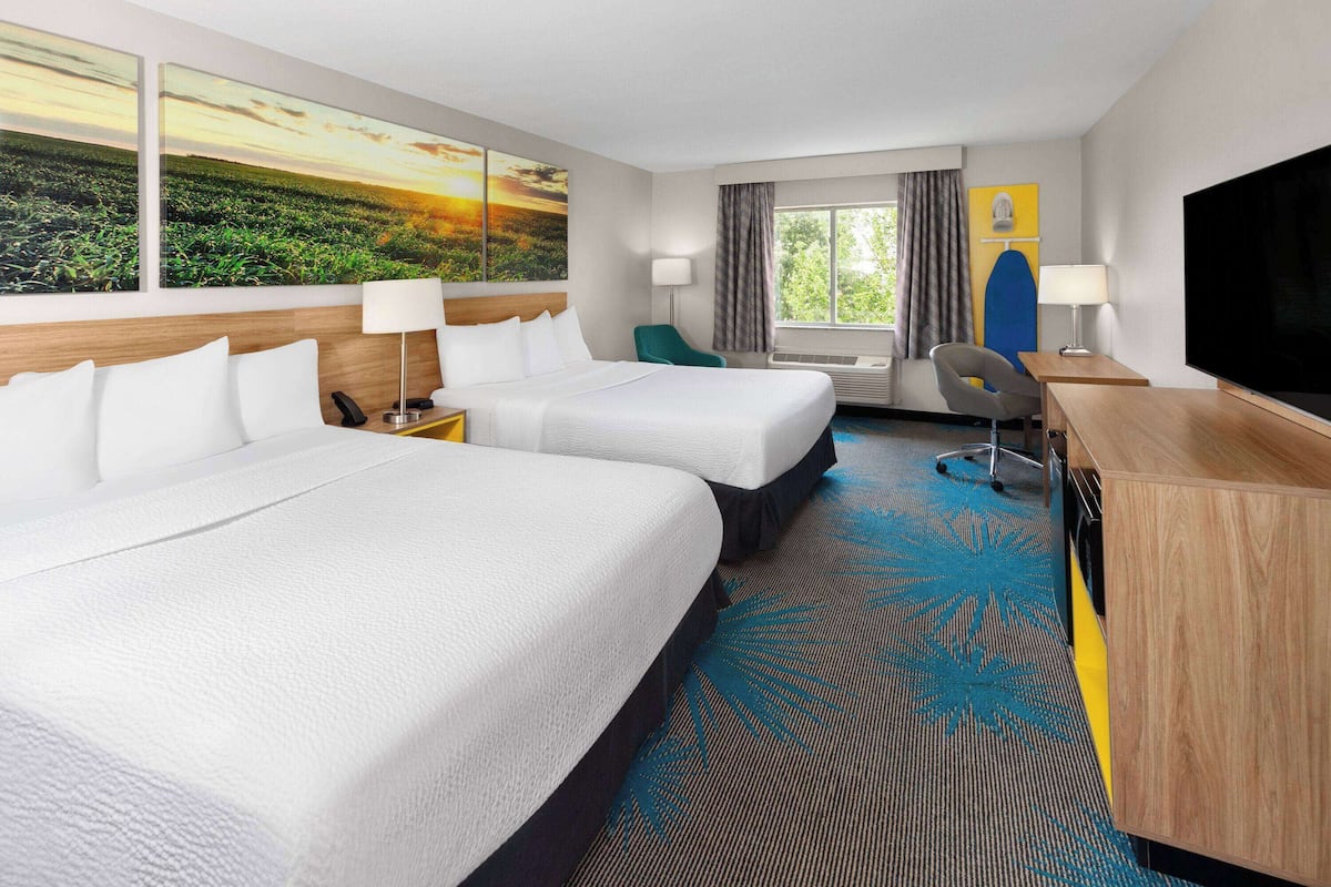 A hotel room with two beds, a desk, a chair, a TV, and a large window.