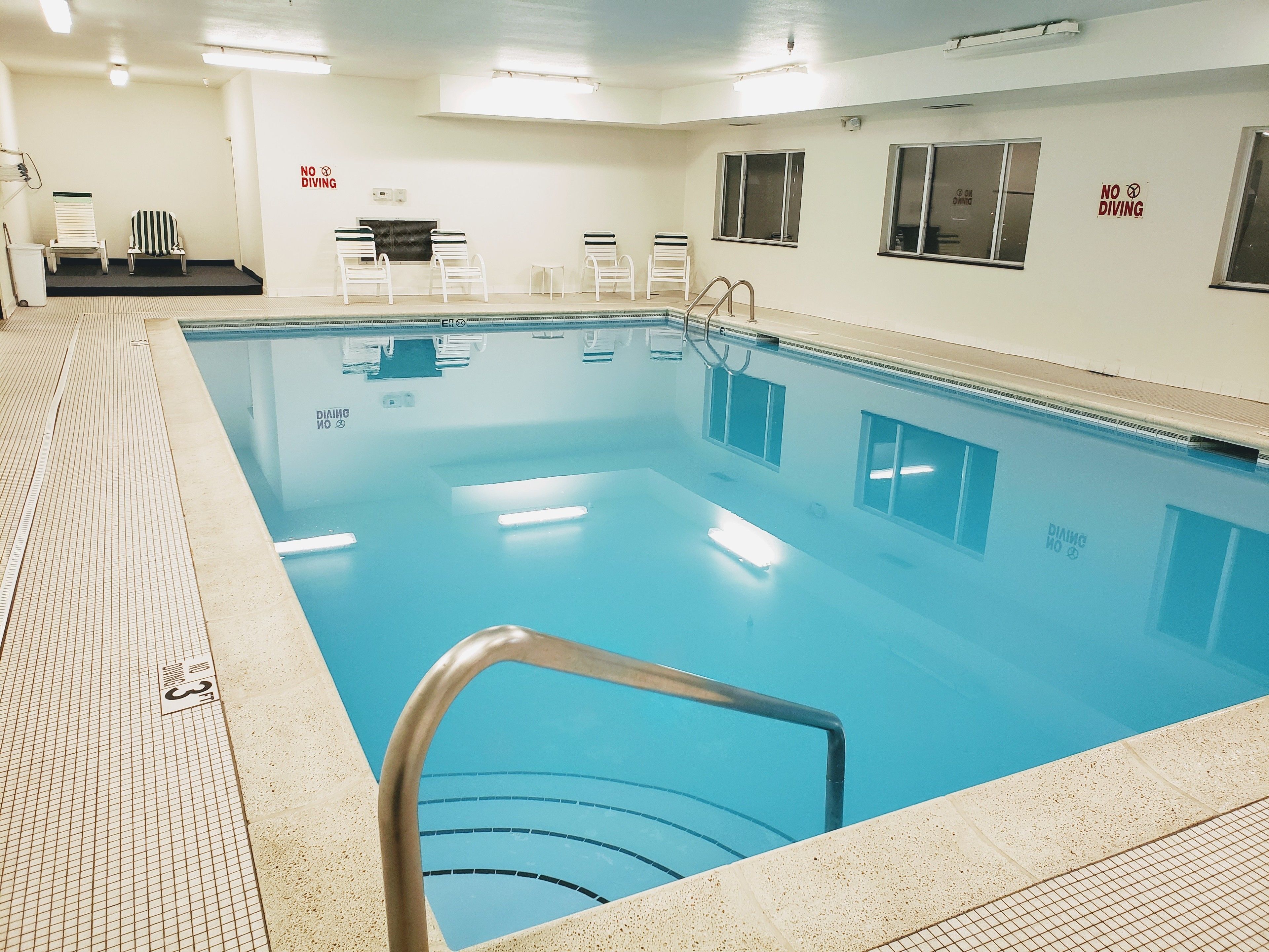 A swimming pool with a tiled deck, a no diving sign, and a few chairs.