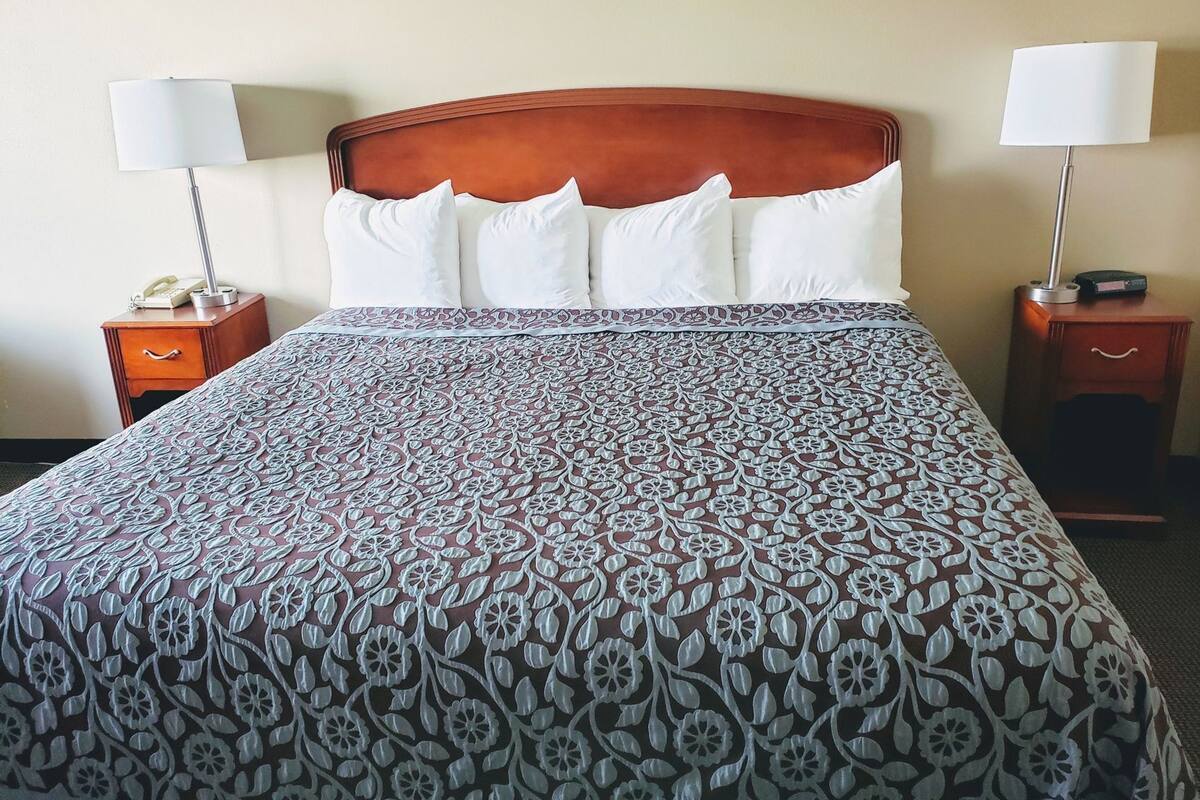 Una habitación de hotel con una cama grande, dos mesitas de noche y lámparas.