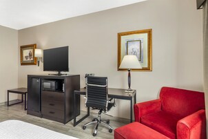 A hotel room with a desk, a red sofa, a TV, a lamp, and two framed pictures on the wall.