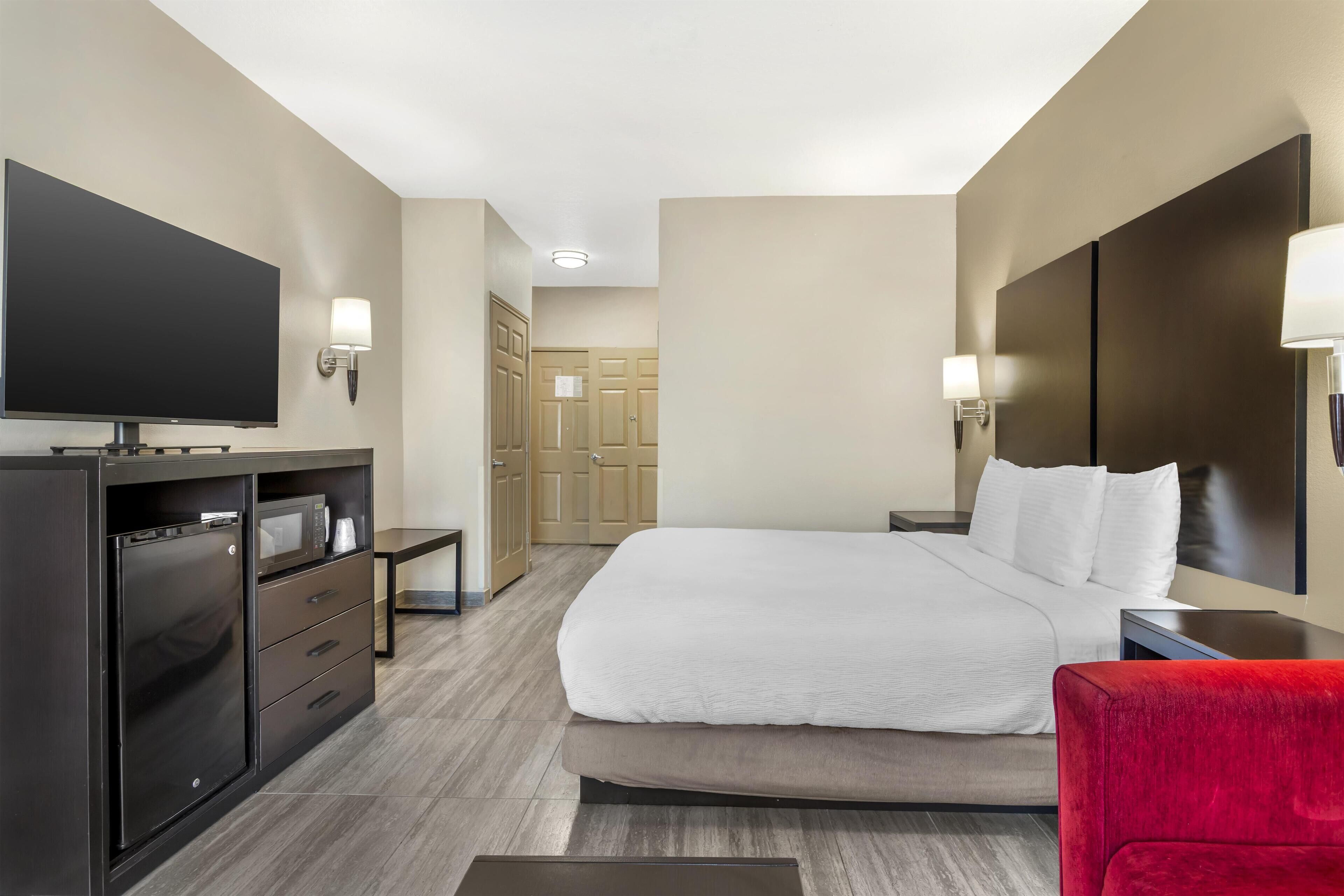Una habitación de hotel con una cama, un televisor, un escritorio y una silla roja.