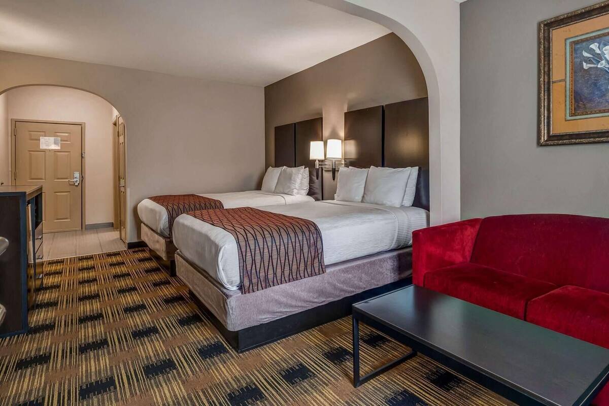 A hotel room with two beds, a red sofa, a small table, and a framed picture on the wall.