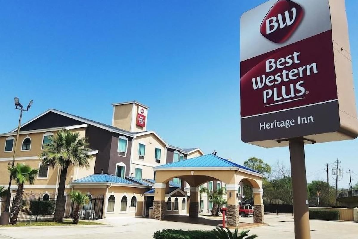 A Best Western PLUS Heritage Inn with a prominent sign, a covered outdoor area, and a building with multiple windows and a blue roof.
