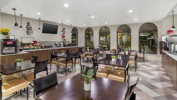 A modern dining area with multiple tables and chairs, a coffee machine, and a counter with a variety of food items. - Best Western Plus Heritage Inn (Houston)