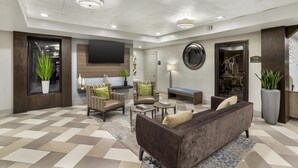 A spacious lobby with a modern design, featuring a large sofa, two armchairs, a coffee table, and a TV mounted on the wall. - Best Western Plus Heritage Inn (Houston)