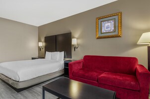 A hotel room with a bed, a red sofa, a small table, and two wall-mounted lamps.