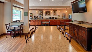 Una cocina de hotel con encimeras de granito, armarios de madera y un televisor de pantalla plana montado en la pared.