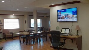 Una sala de conferencias con una larga mesa, varias sillas, un ordenador portátil sobre un escritorio y una televisión en la pared mostrando un programa de viajes.