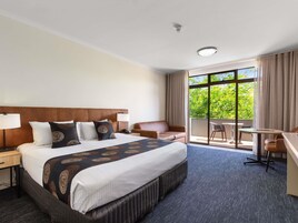 A hotel room with a large bed, a desk, a chair, and a balcony with a view.