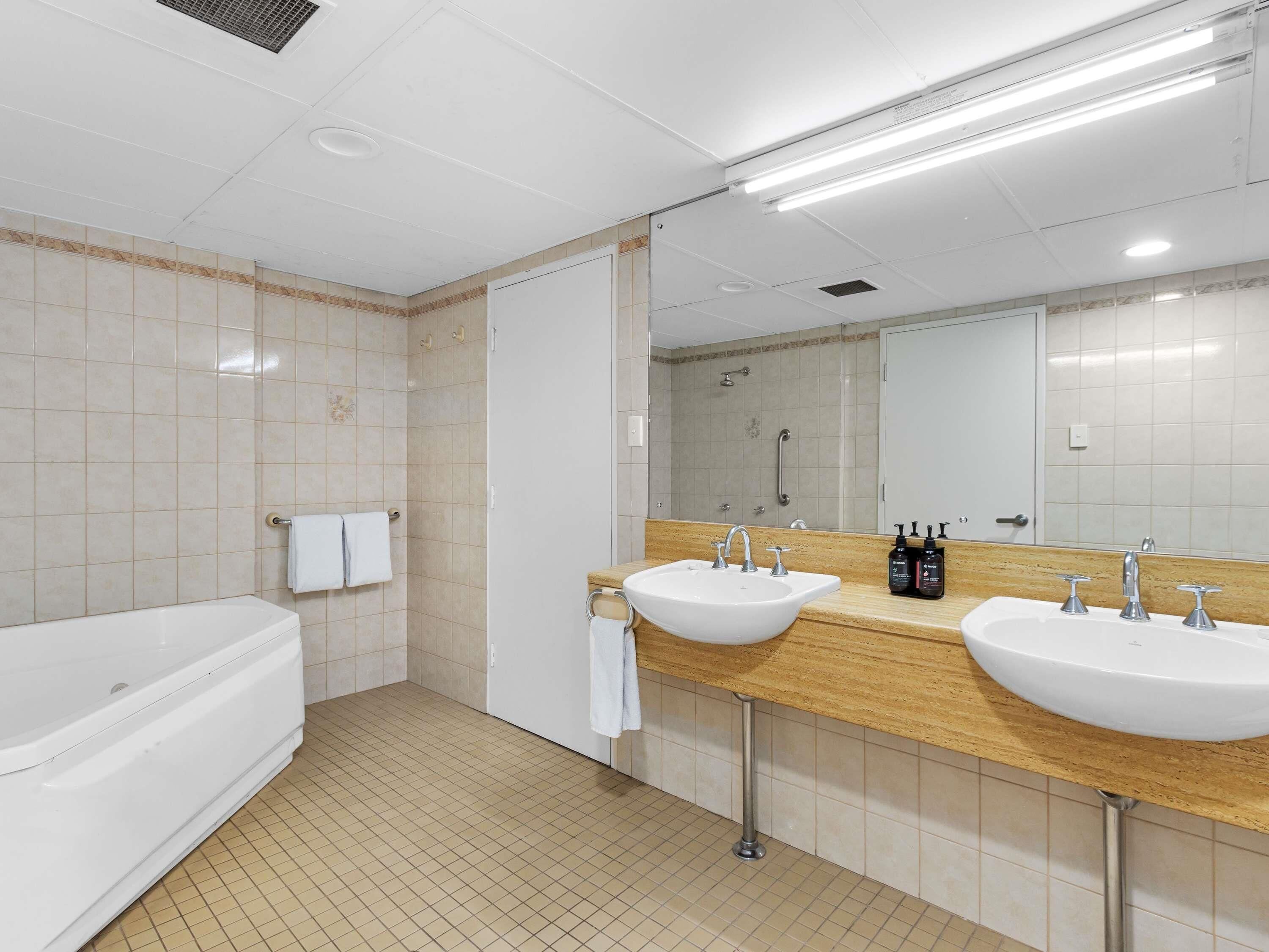 Un baño moderno con dos lavamanos, una bañera y una ducha.
