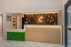 Balcão de recepção de hotel com acabamento em madeira e uma planta artificial verde.