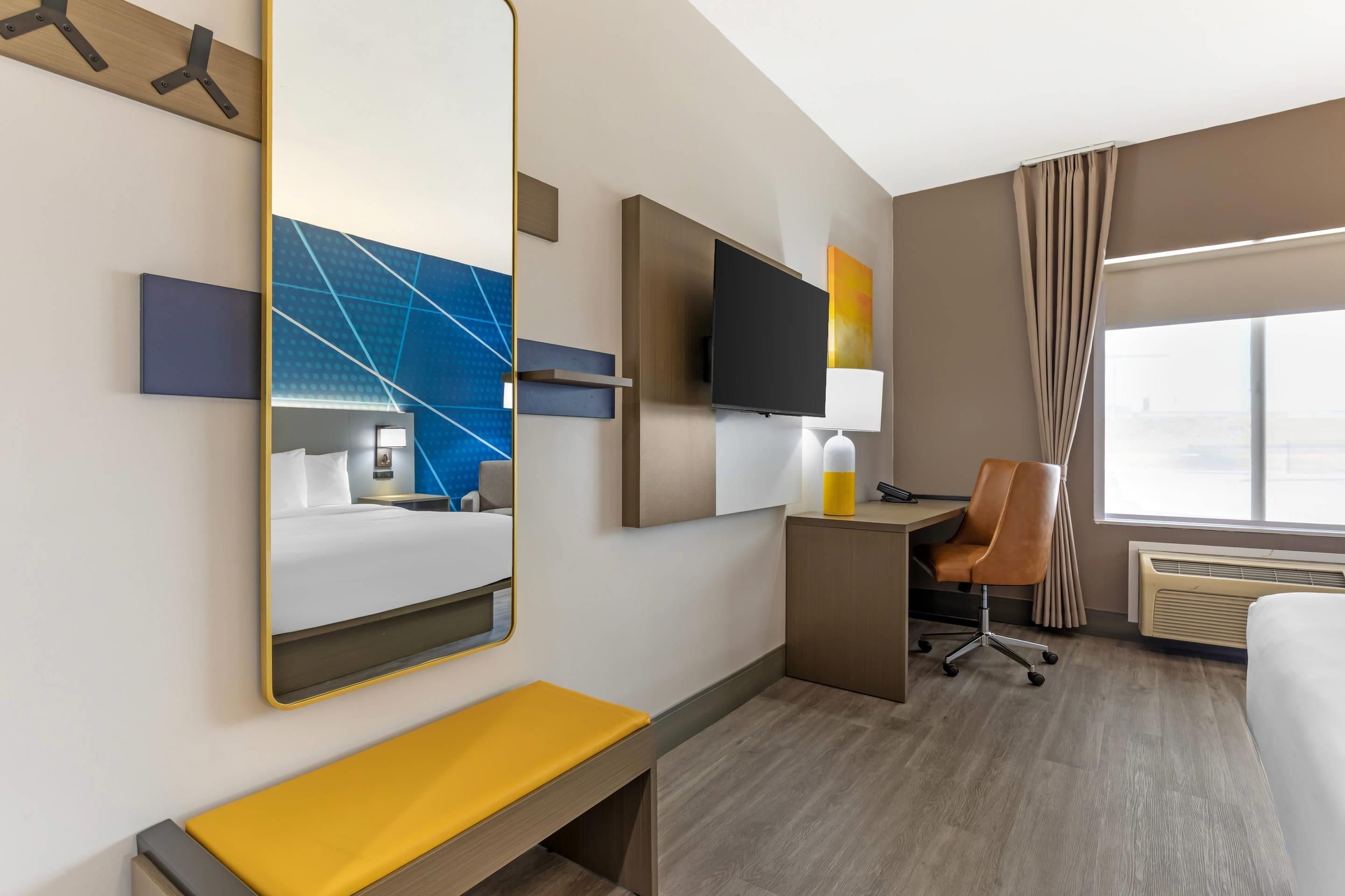 A hotel room with a bed, a desk, a chair, a TV, and a large window.