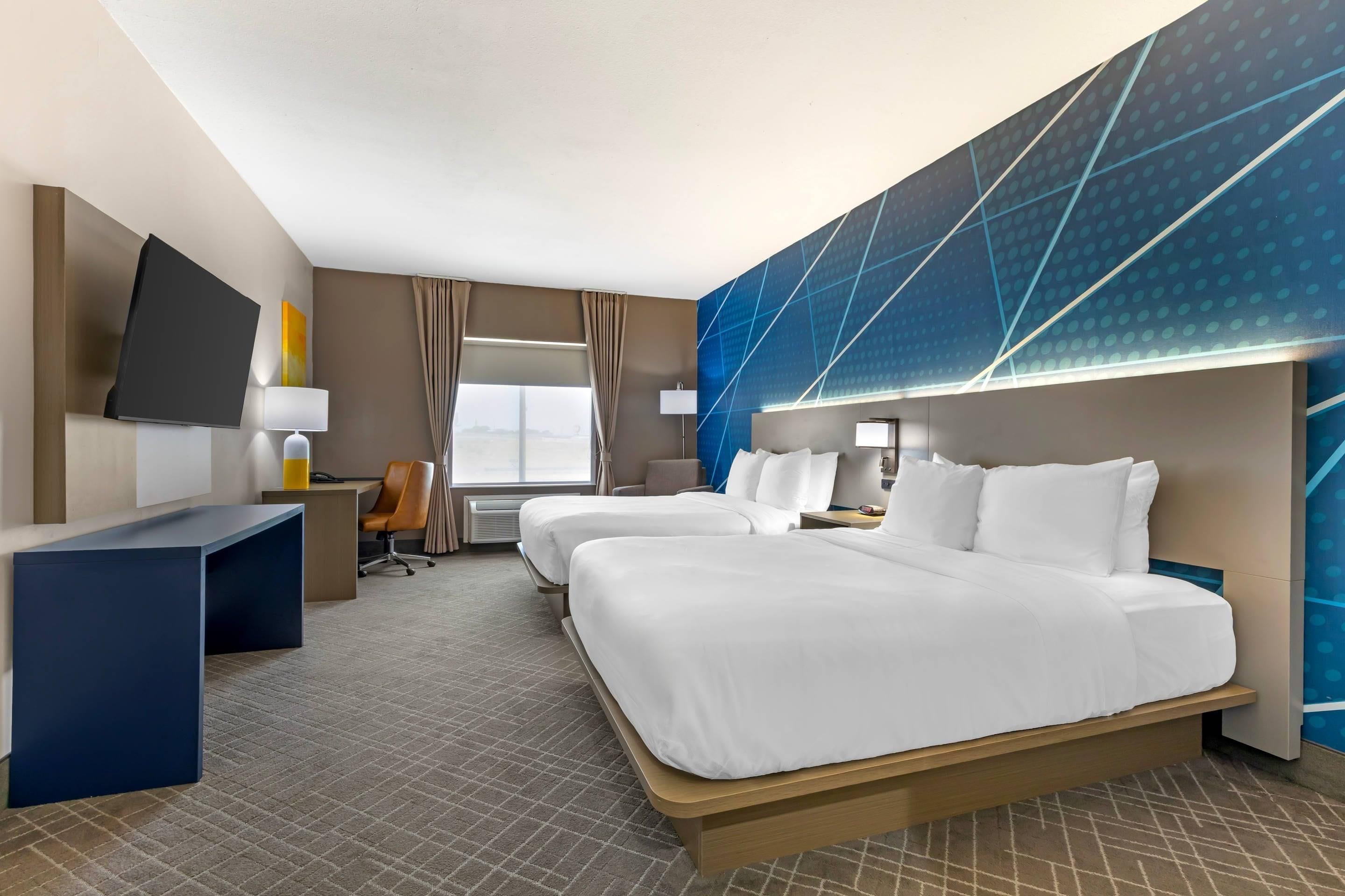 A hotel room with a large bed, a desk, a chair, a TV, and a window with curtains.