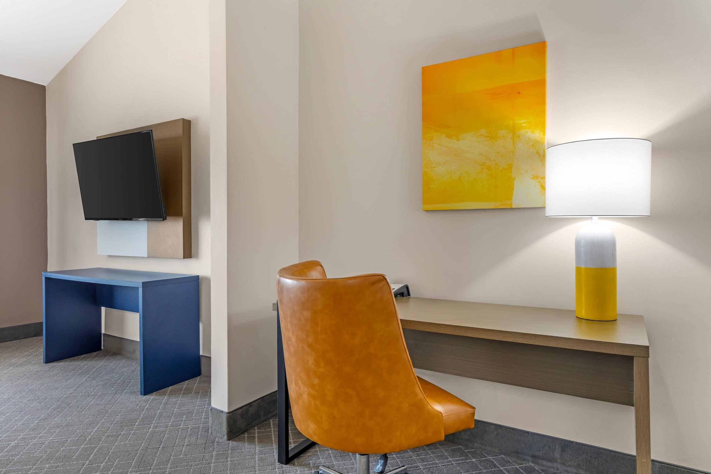 Een hotelkamer met een bureau, stoel, televisie en een lamp.