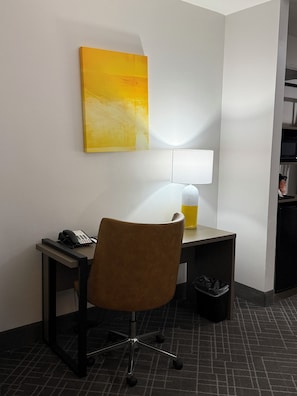 Una camera d'albergo con scrivania, sedia, lampada e un quadro appeso al muro.