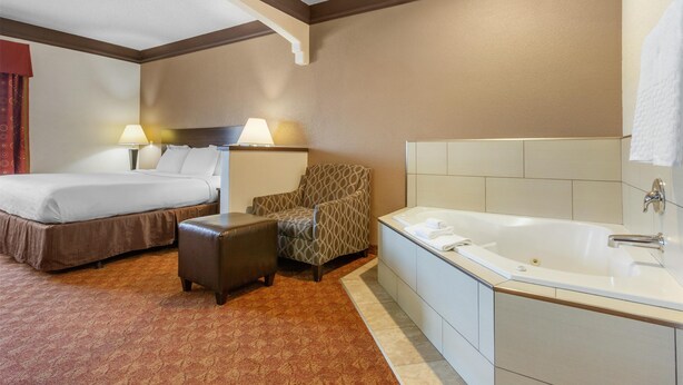 A hotel room with a bed, a chair, a small ottoman, and a bathtub. - Best Western Tolleson Hotel (Tolleson)