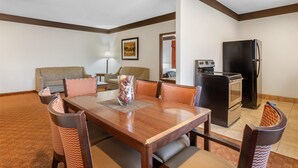 A hotel room with a dining area featuring a wooden table and chairs, a sofa, a small kitchenette with a refrigerator and stove, and a mirror on the wall. - Best Western Tolleson Hotel (Tolleson)