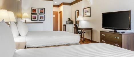 A hotel room with two beds, a desk, a television, and framed pictures on the wall.