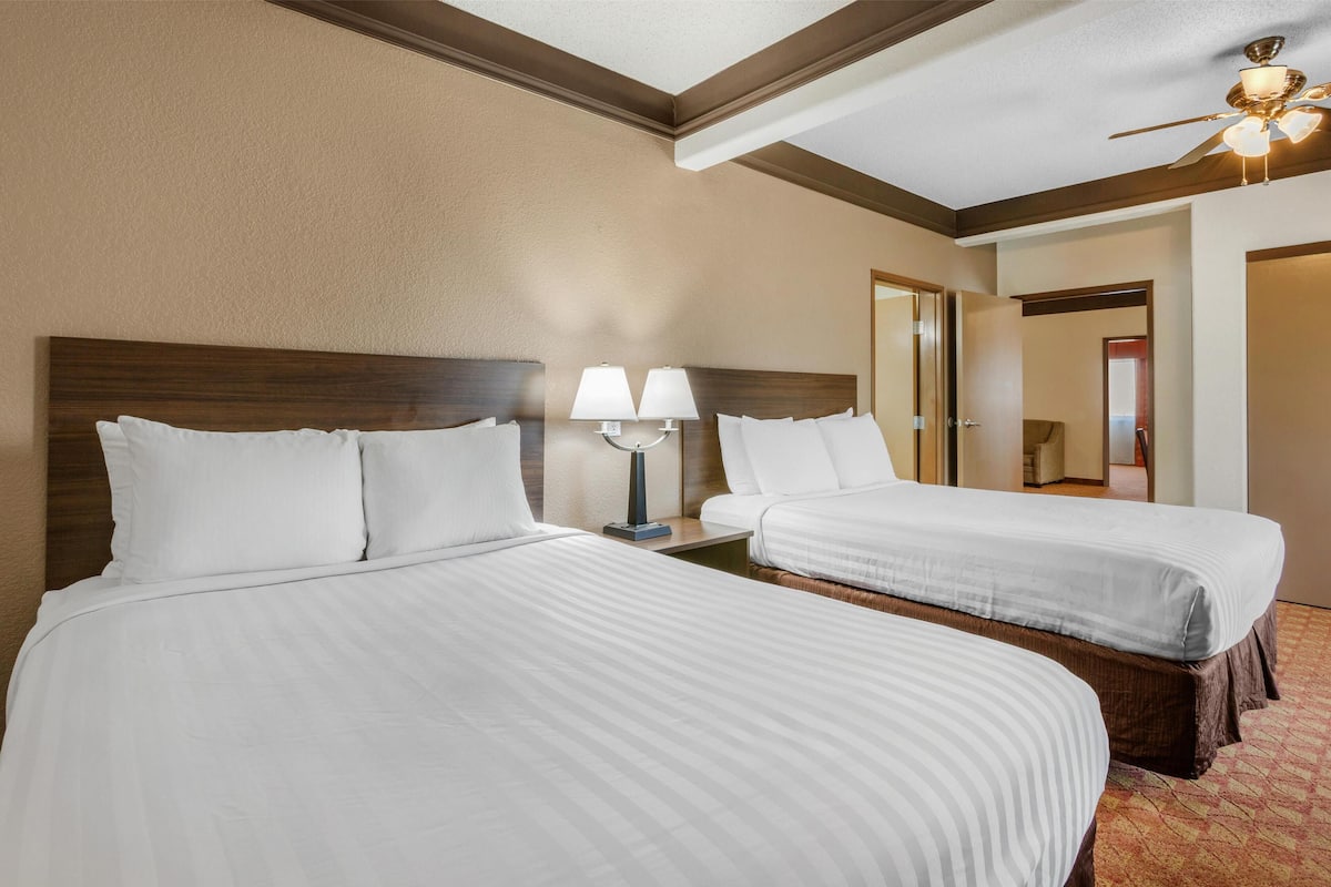 Ein Hotelzimmer mit zwei Betten, einem Nachttisch mit Lampen, einem Deckenventilator und einem Spiegel an der Wand.