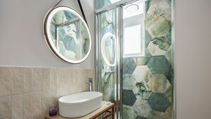 Casa de banho com um espelho redondo, uma pia branca e um chuveiro com azulejos hexagonais.