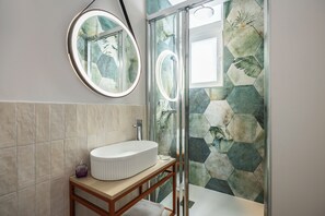 A bathroom with a round mirror, a white sink, and a shower with hexagonal tiles.