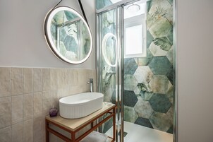 A bathroom with a round mirror, a white sink, and a shower with hexagonal tiles.