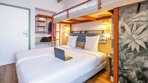 Uma cama de casal com um laptop, uma prateleira de madeira com toalhas e uma luminária na parede.