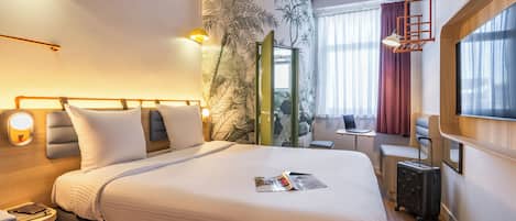 A hotel room with a large bed, a desk, a laptop, and a suitcase.