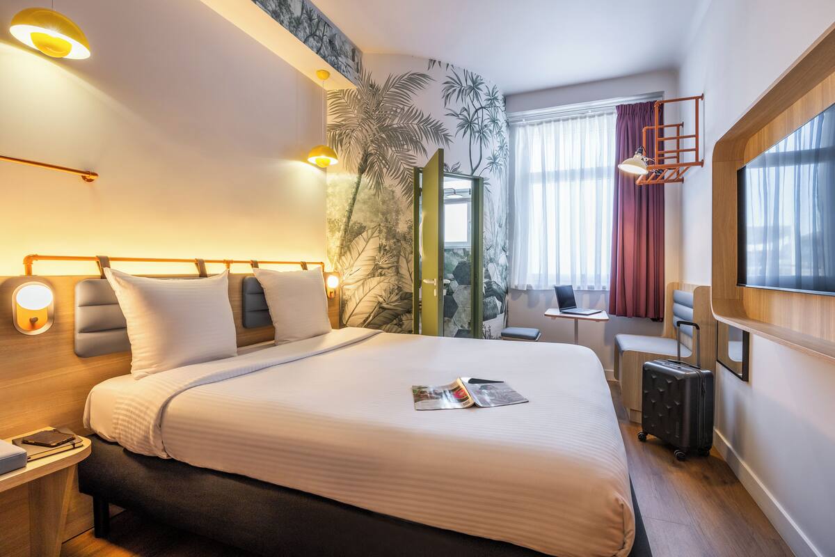 A hotel room with a large bed, a desk, a laptop, and a suitcase.