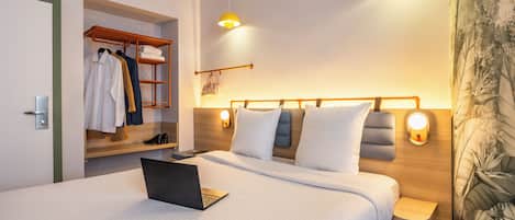 Una habitación de hotel moderna con una cama bien hecha, un ordenador portátil sobre la cama, un cabecero de madera y un armario empotrado.