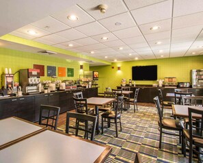 A hotel restaurant with a green wall, a coffee bar, and multiple tables and chairs. - Comfort Inn & Suites Lantana - West Palm Beach South (Lantana)