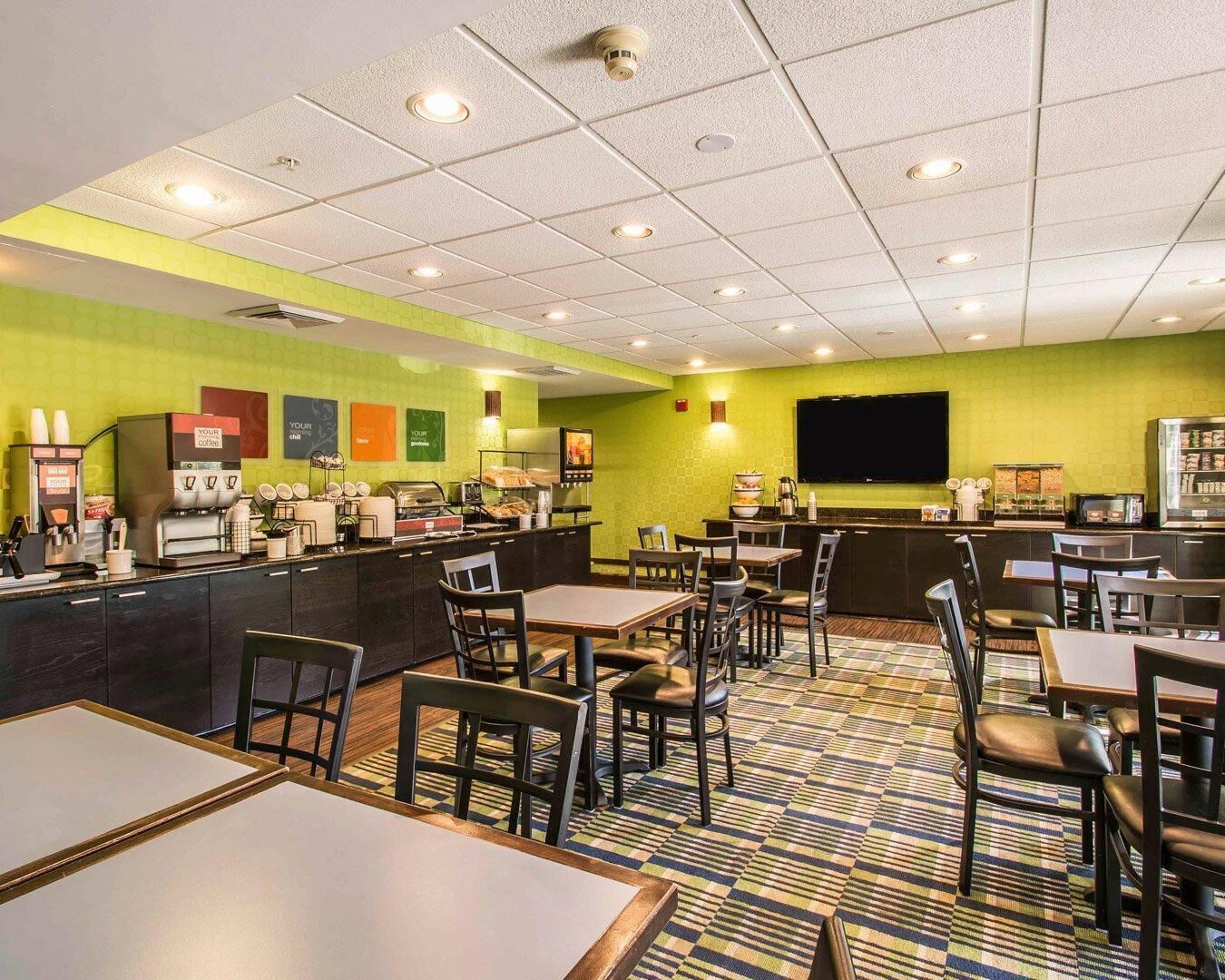 A hotel restaurant with a bar area, seating, and a television screen.
