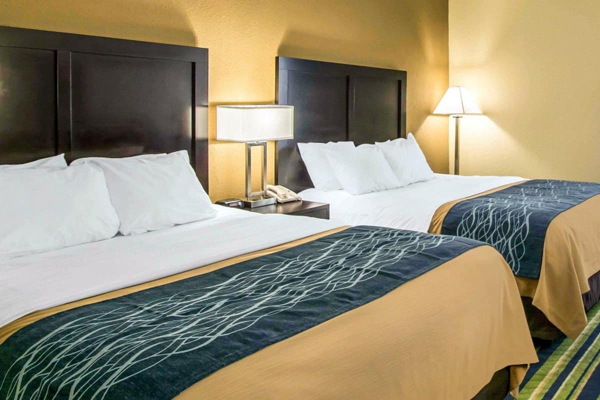 Habitación de hotel con dos camas, cada una con cabecera, mesita de noche con lámpara y teléfono.